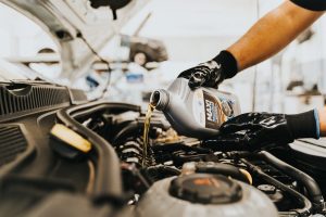 Avaleht Close-up of a mechanic pouring engine oil into a car engine in an auto repair shop.