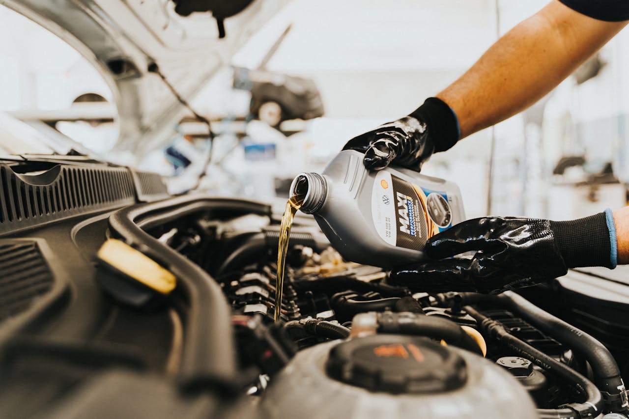 Avaleht Close-up of a mechanic pouring engine oil into a car engine in an auto repair shop.