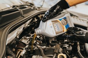 Avaleht A mechanic wearing gloves pouring oil into a car engine in a garage setting.