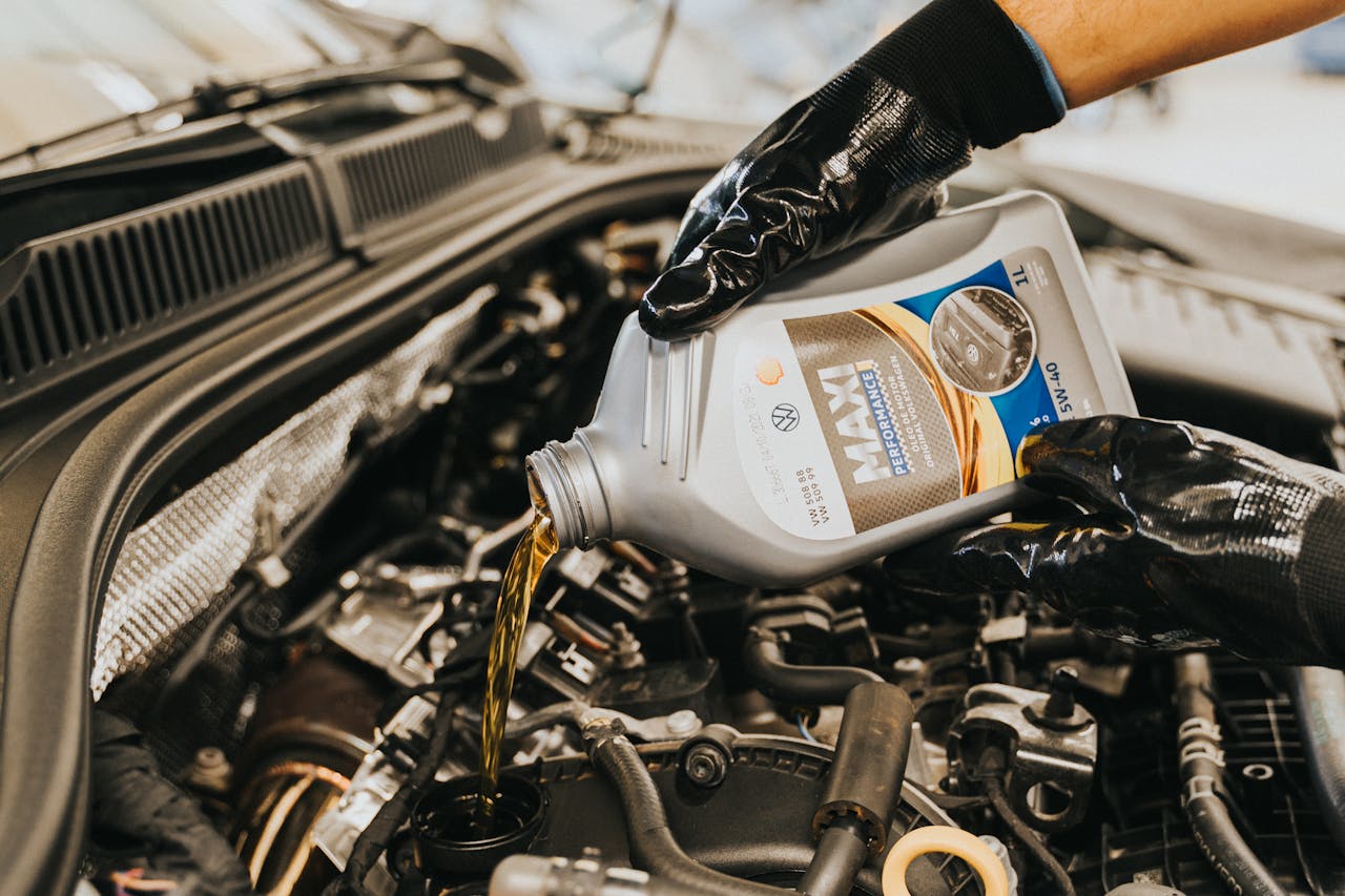 Avaleht A mechanic wearing gloves pouring oil into a car engine in a garage setting.