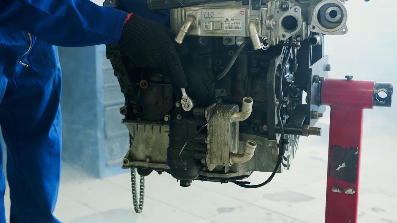 Avaleht Mechanic wearing gloves uses a wrench to fix a car engine in a workshop.